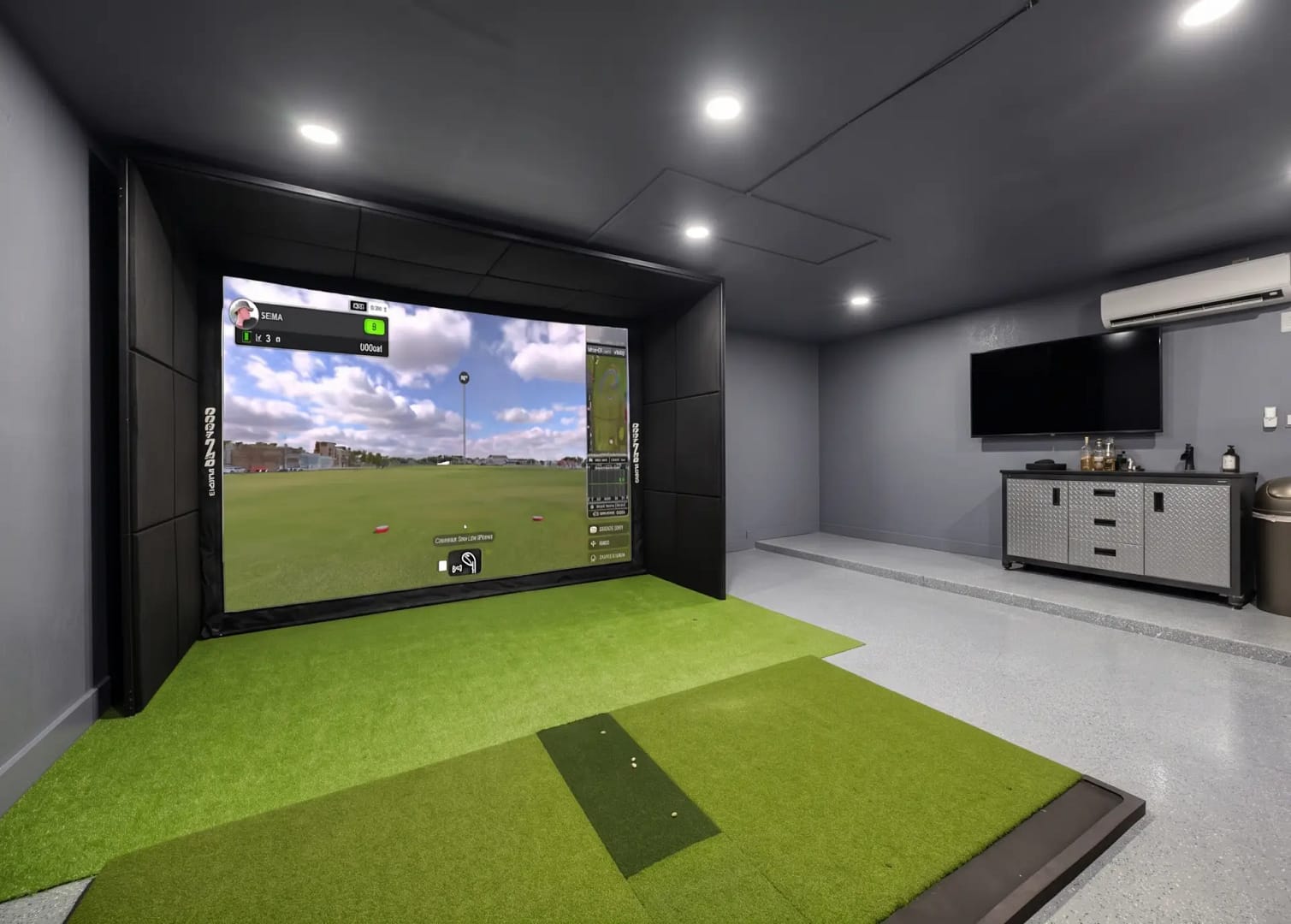 A modern industrial garage golf simulator in St. Petersburg, Florida, featuring matte grey acoustic wall padding, custom diamond-plate cabinetry, and recessed LED ceiling lighting for a professional home practice environment.