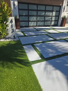 Modern-Tampa-Driveway-Turf-Paver-strips - Sims & Greens Modern Tampa home entrance featuring geometric concrete pavers with artificial turf strips and a frosted glass garage door.