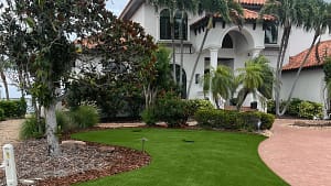 St-Pete-Beach-FL-Artificial-Turf-Lawn-Replacement - Sims & Greens Luxury coastal home in St. Pete Beach, Florida, featuring a full synthetic lawn replacement with salt-resistant artificial turf and tropical landscaping.