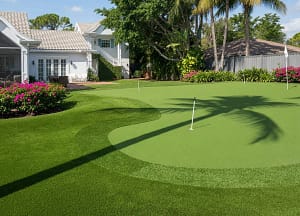 Clearwater FL Backyard Putting Green | Luxury Artificial Turf Golf Green - Sims & Greens Luxurious backyard putting green made with bright green artificial turf in Clearwater, Florida. Smooth rolling contours, white flagstick, palm tree shadows, and upscale residential home in the background. Perfect for home golf simulator practice.